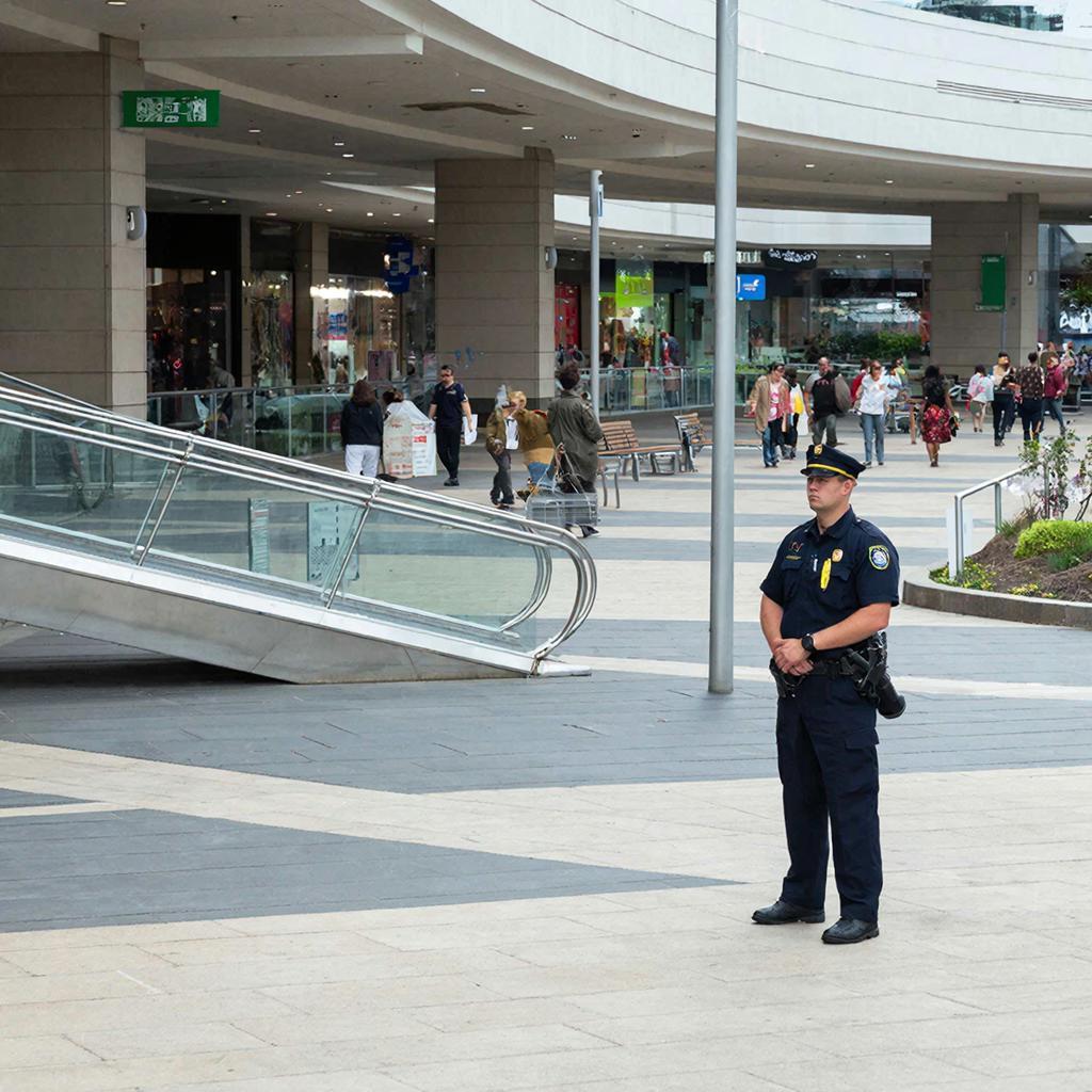 Современный торговый центр, охранник внимательно наблюдает за обстановкой, люди спешат за кпокупками